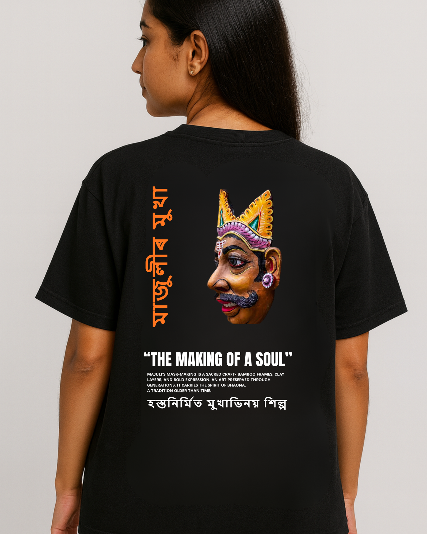 Assam Majuli mask-making artwork T-shirt — Assamese text and Bhaona mask graphic on black oversized tee (female model).
